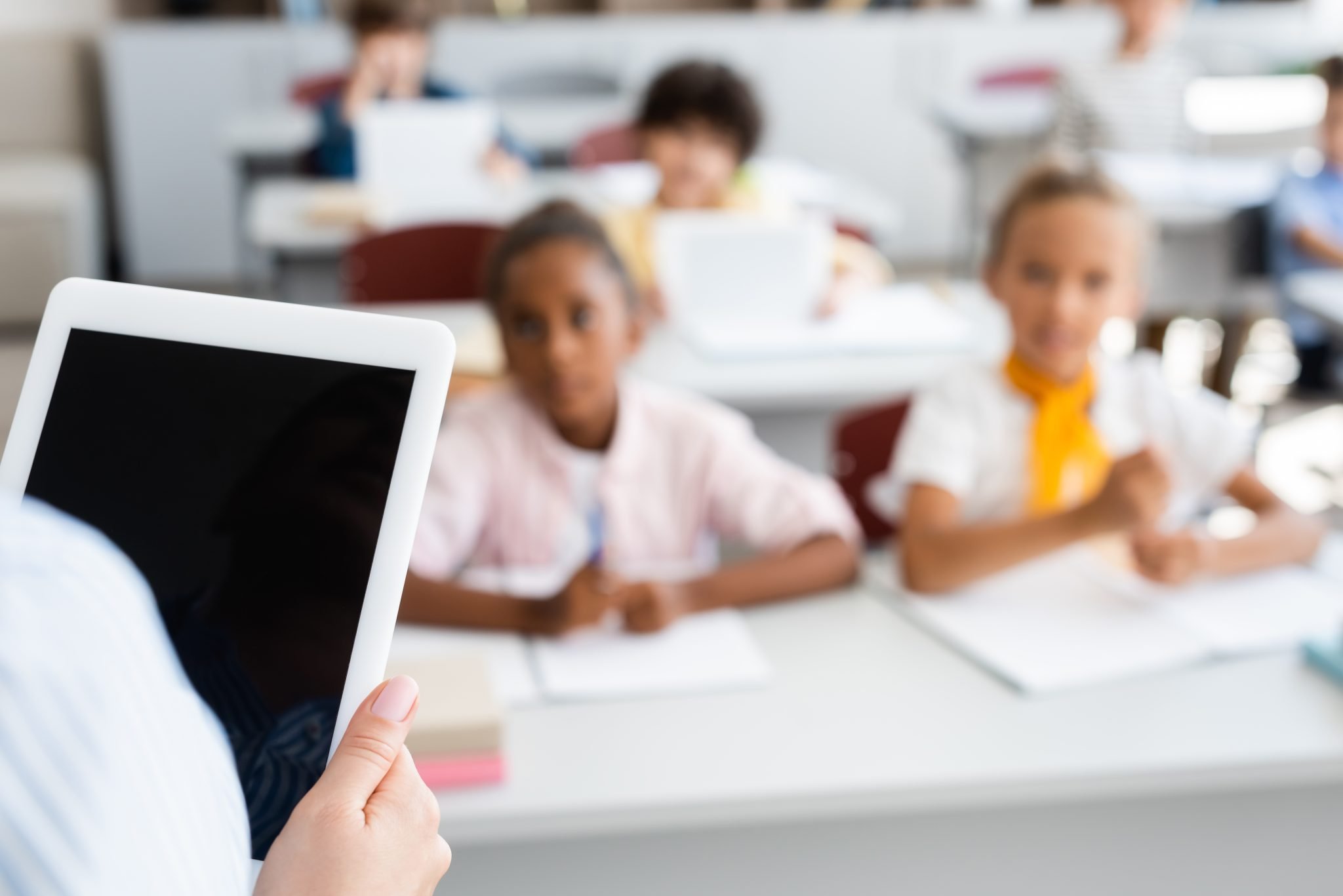 cropped view of teacher holding digital tablet with blank screen near multiethnic pupils