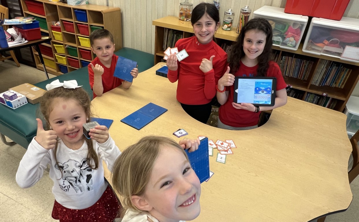 happy students with their kaibots and coding cards. One girl is holding a tablet displaying Kainundrum Lite app